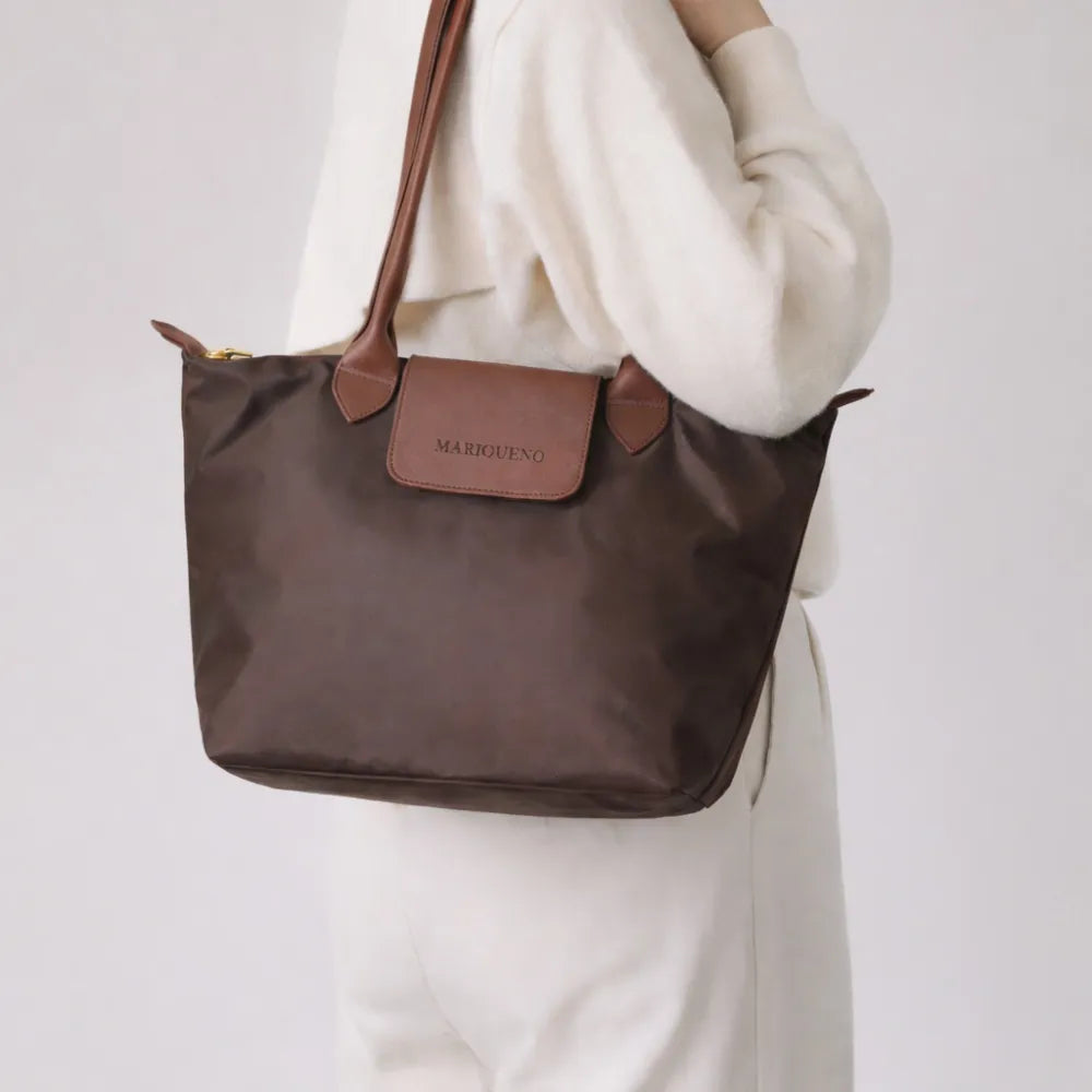 Brown handbag with leather accents held by a person wearing a white outfit on a light gray background
#color_choco brown