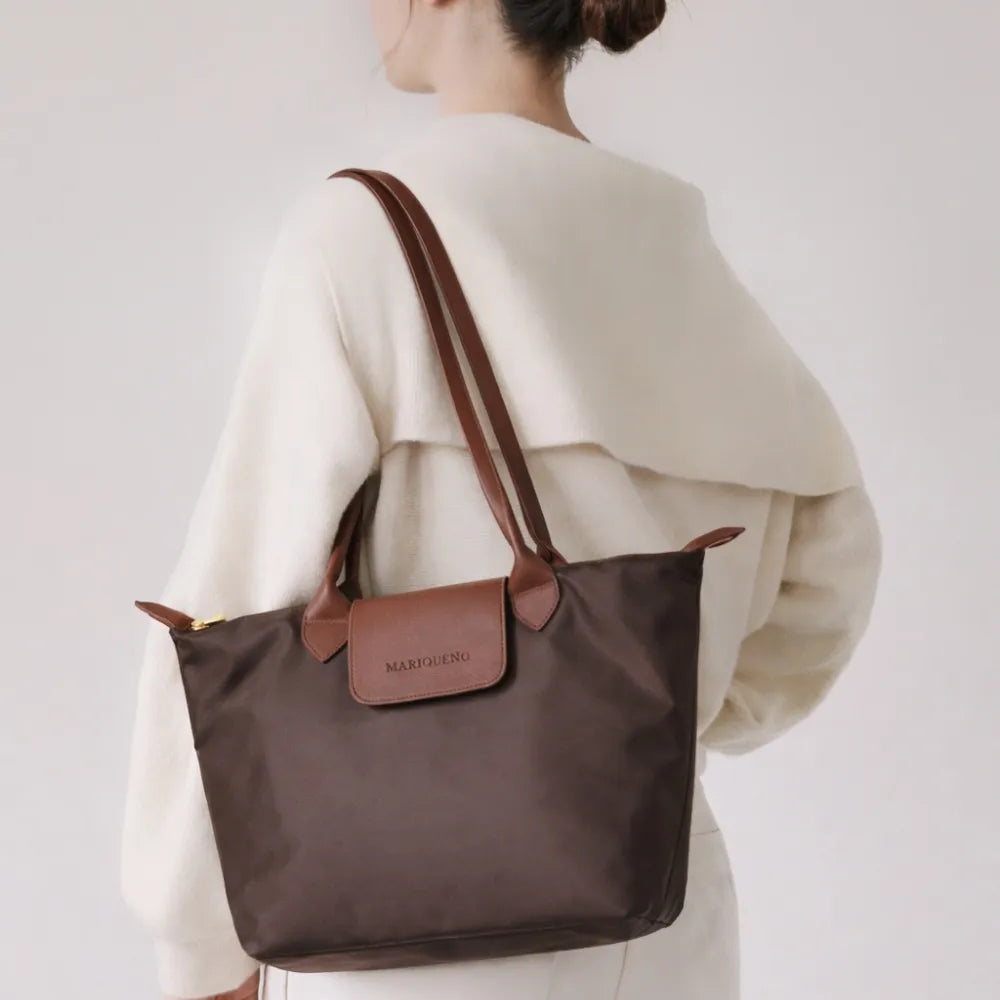 Person wearing a brown tote bag with a visible brand logo on a plain 
background
#color_choco brown