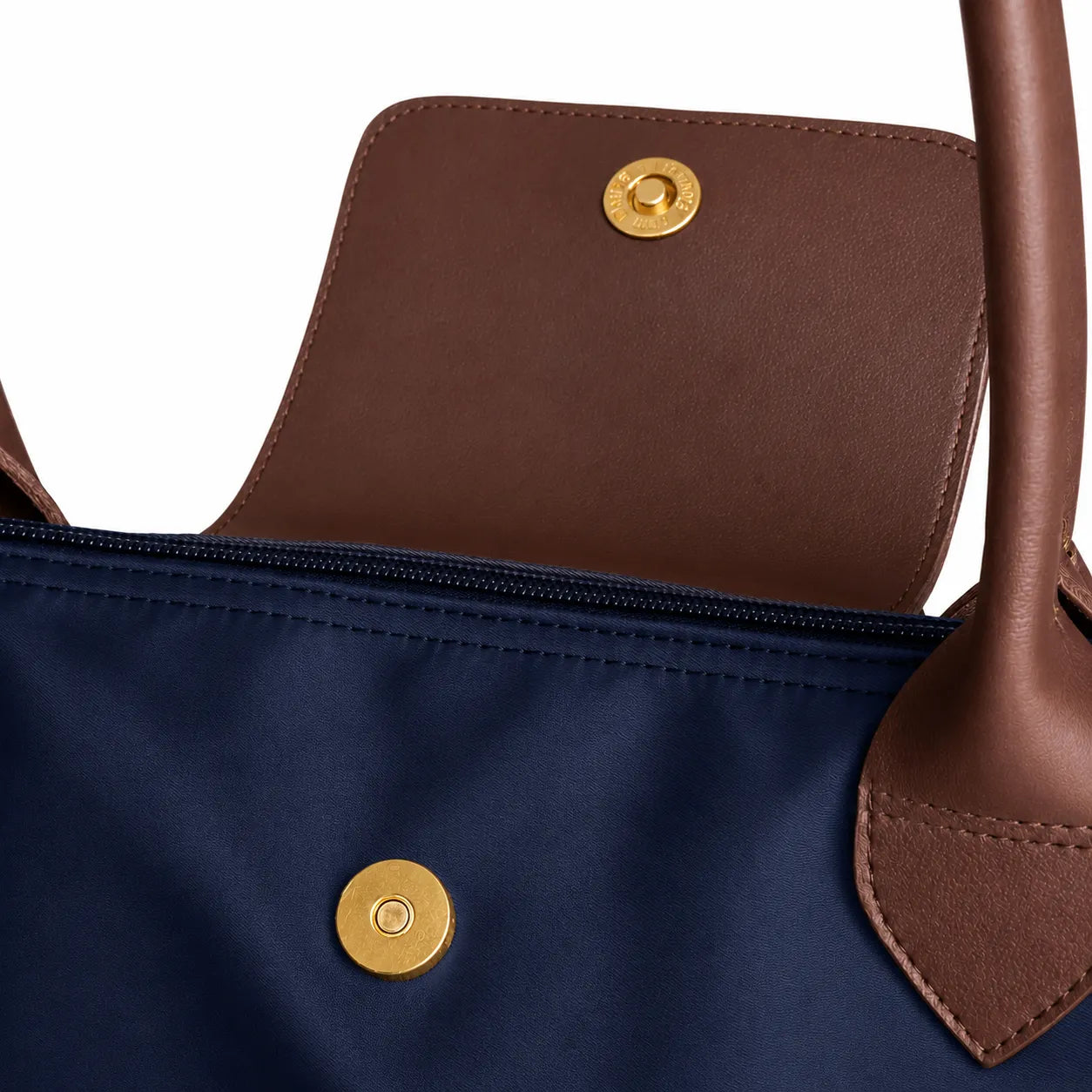 Close-up of a navy blue bag with brown leather handles and gold buttons on a white background
#color_navy blue