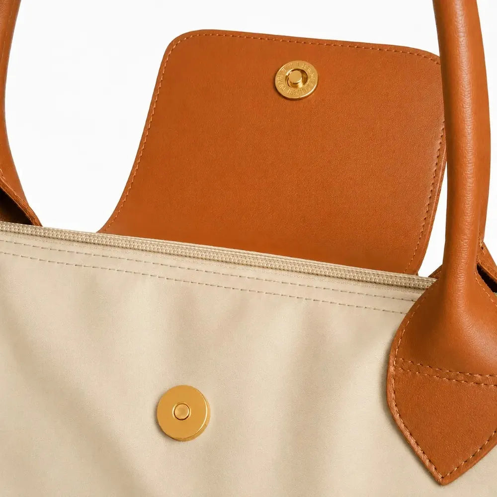 Close-up of a bag with brown leather straps and a taupe fabric body featuring a gold button.
#color_taupe