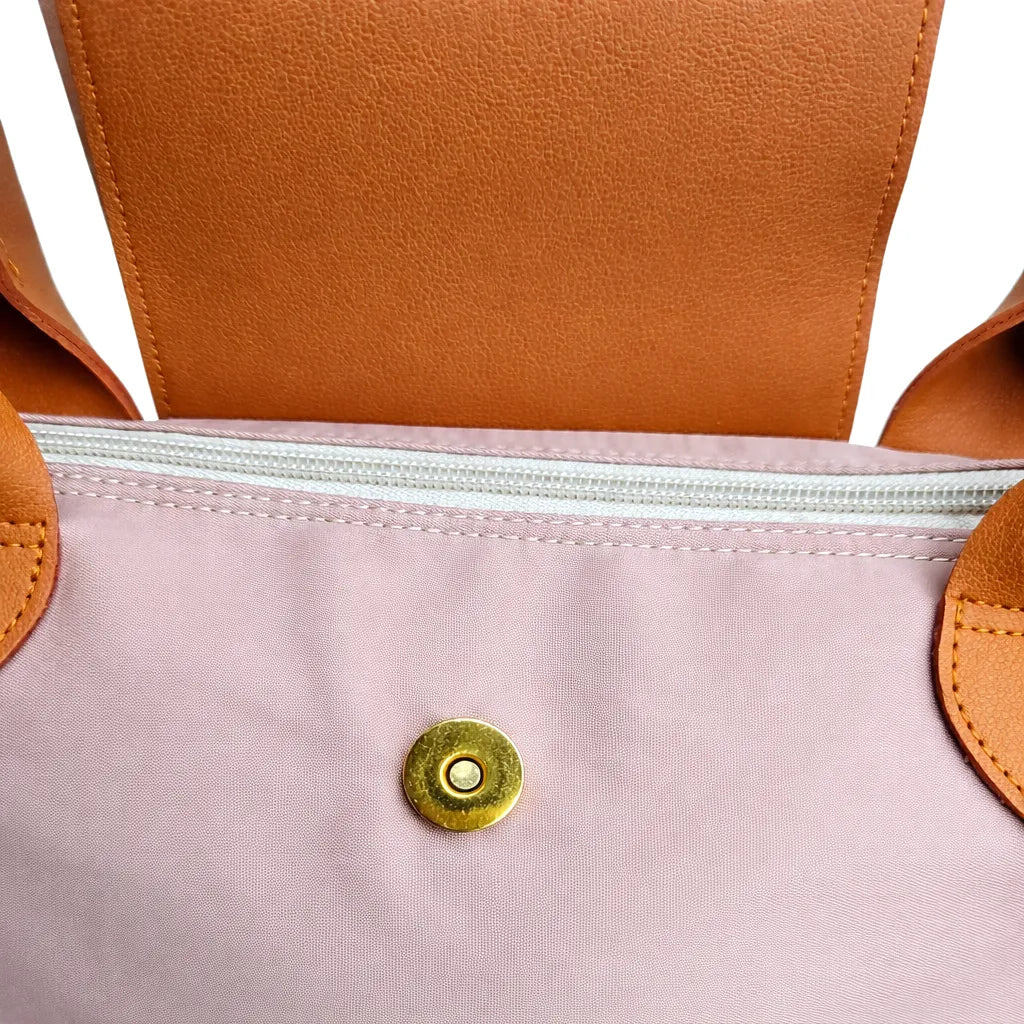 Close-up of a bag with brown leather straps and a taupe fabric body featuring a gold button.
#color_taupe