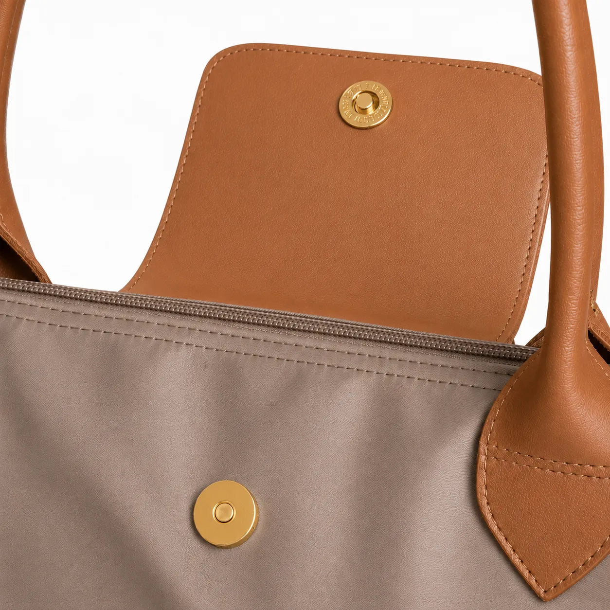 Close-up of a bag with brown leather straps and a taupe fabric body featuring a gold button.
#color_taupe