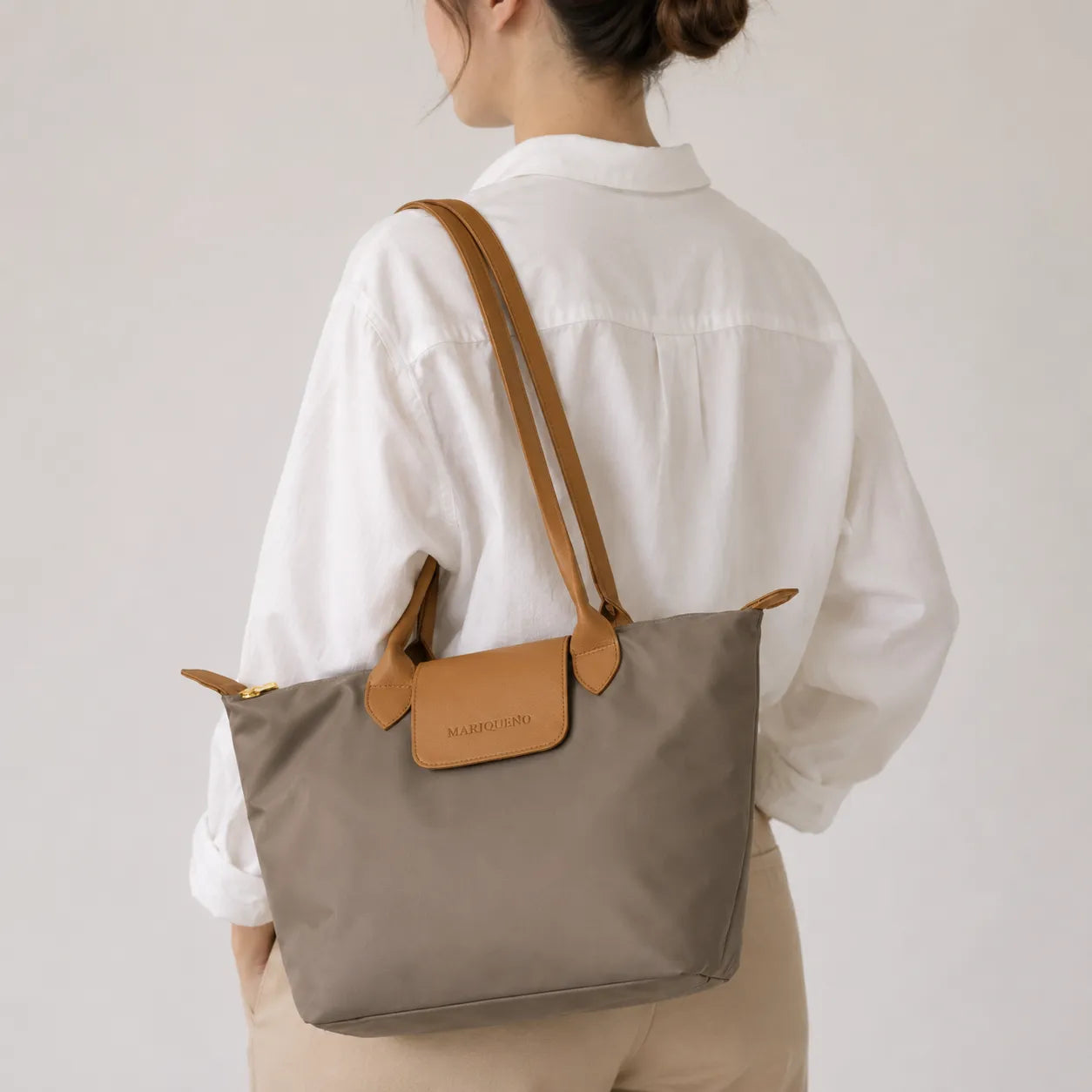Taupe tote bag with brown leather accents held by a person against a gray background
#color_taupe