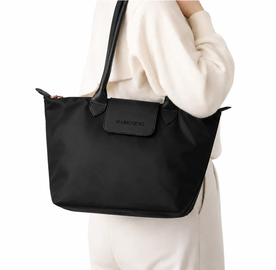A black nylon tote bag with a leather-look front flap and shoulder straps, worn by a person in a cream-colored sweater. The brand name 'MARIQUENO' is embossed on the front flap.
#color_triple black