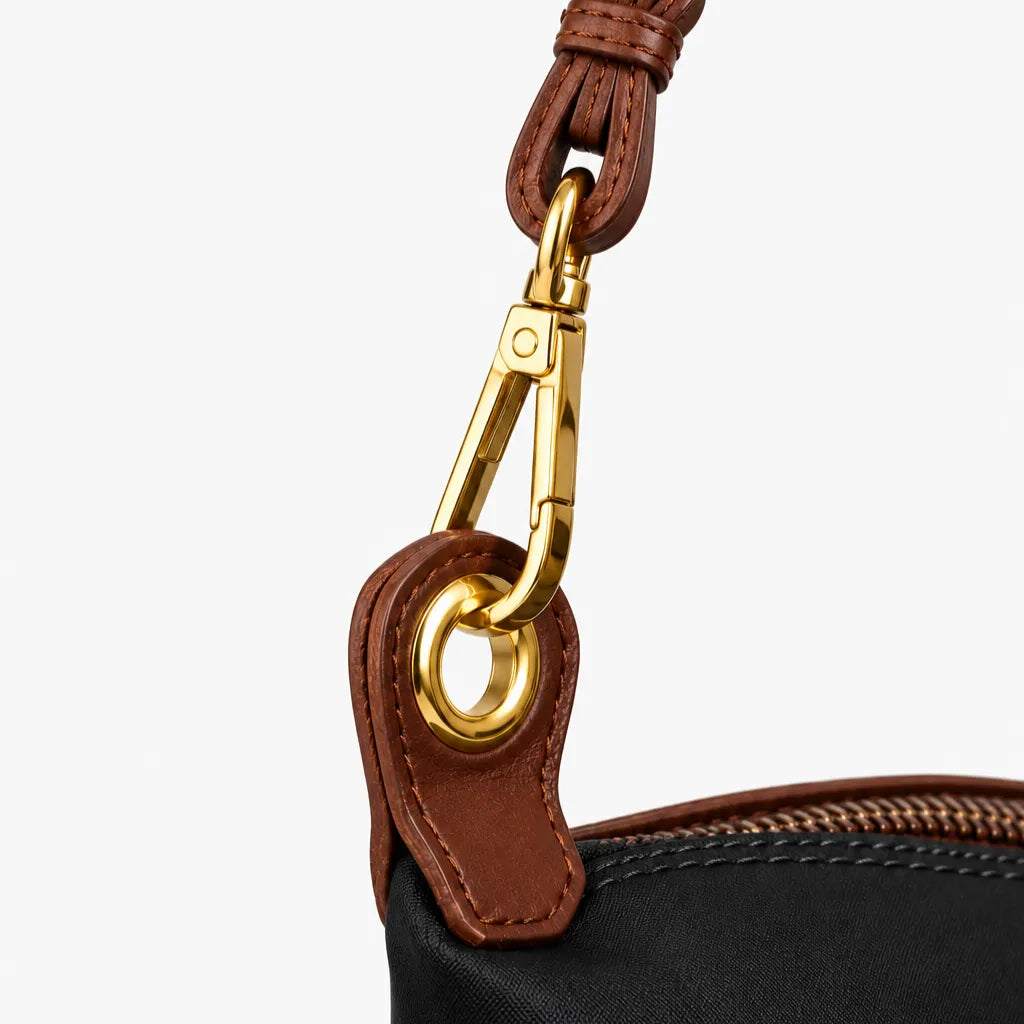 Close-up of a black fabric bag with brown leather trim and a gold-tone metal clasp attachment on a light gray background.
#color_black and choco