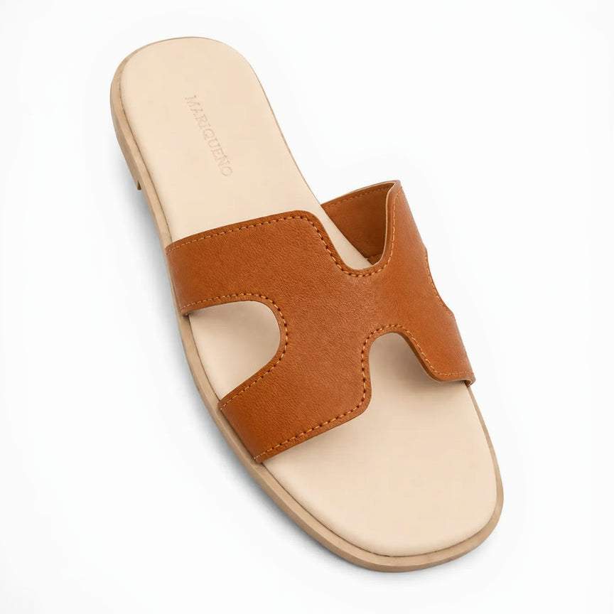 A single slide sandal with a wide, double cutout strap in a warm cognac brown, set on a light beige footbed with the brand name 'MARIQUEÑO' printed on the insole, photographed on a clean white background.
#color_tan