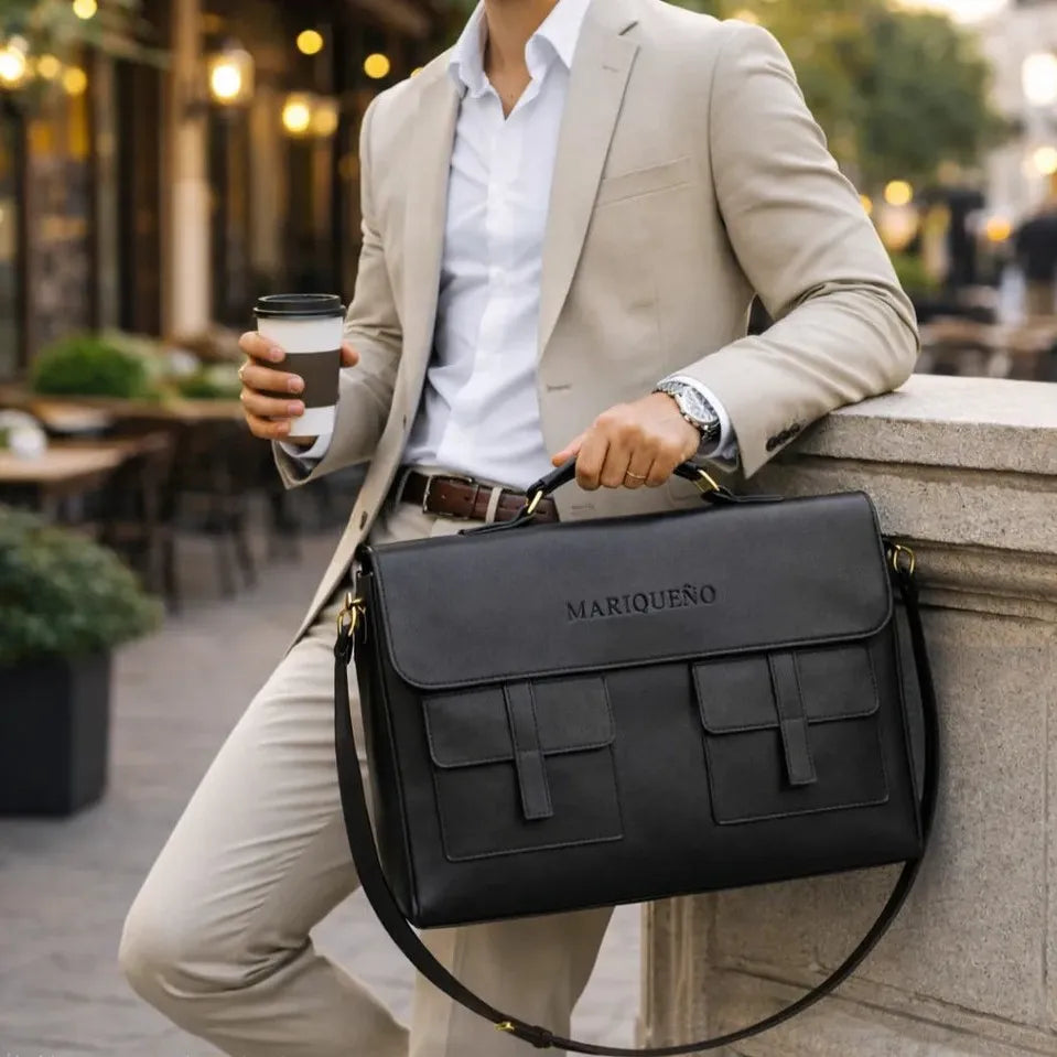 Man in a suit holding a black leather bag with 'Marqueno' branding outdoors.