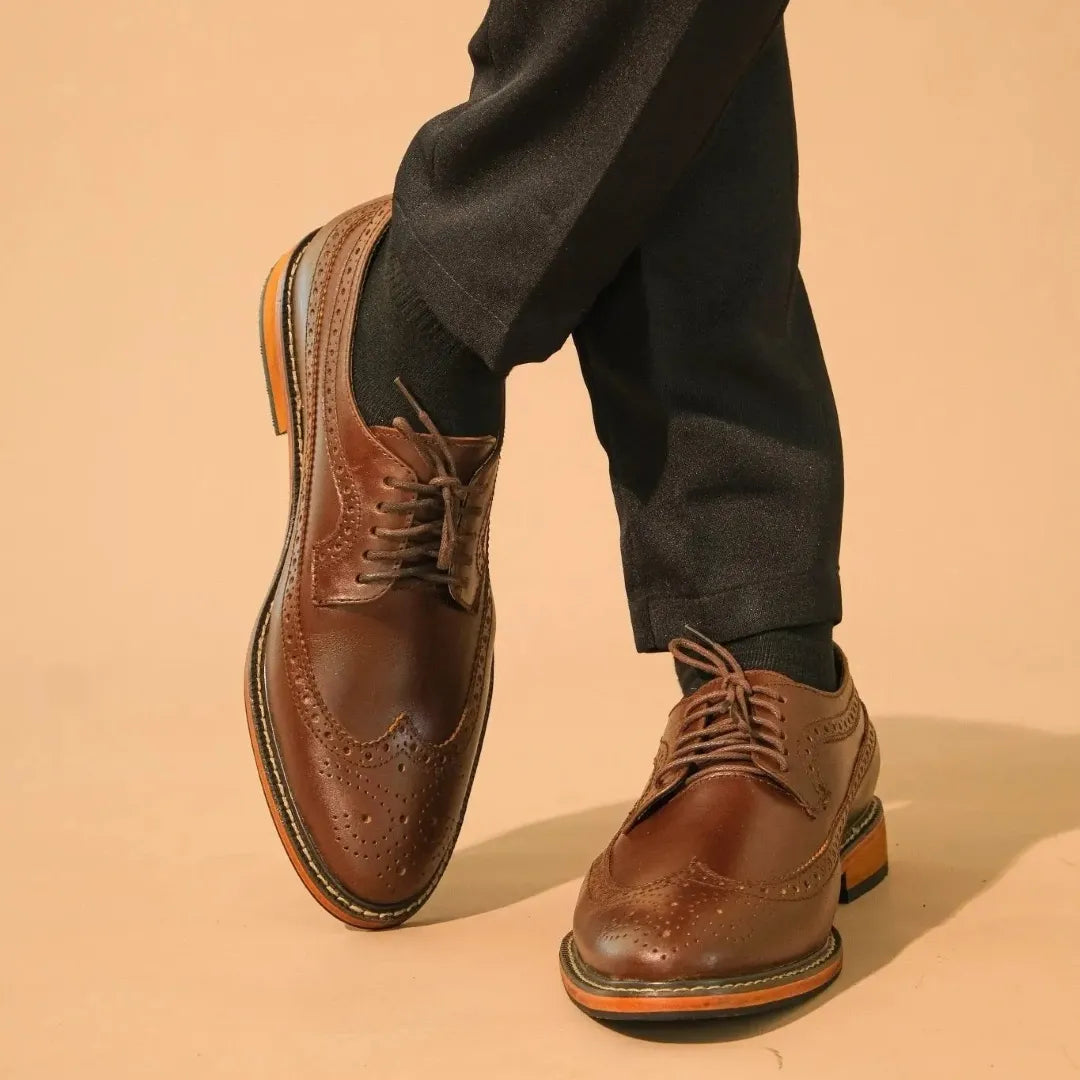 Brown leather dress shoes worn with black pants on a beige background