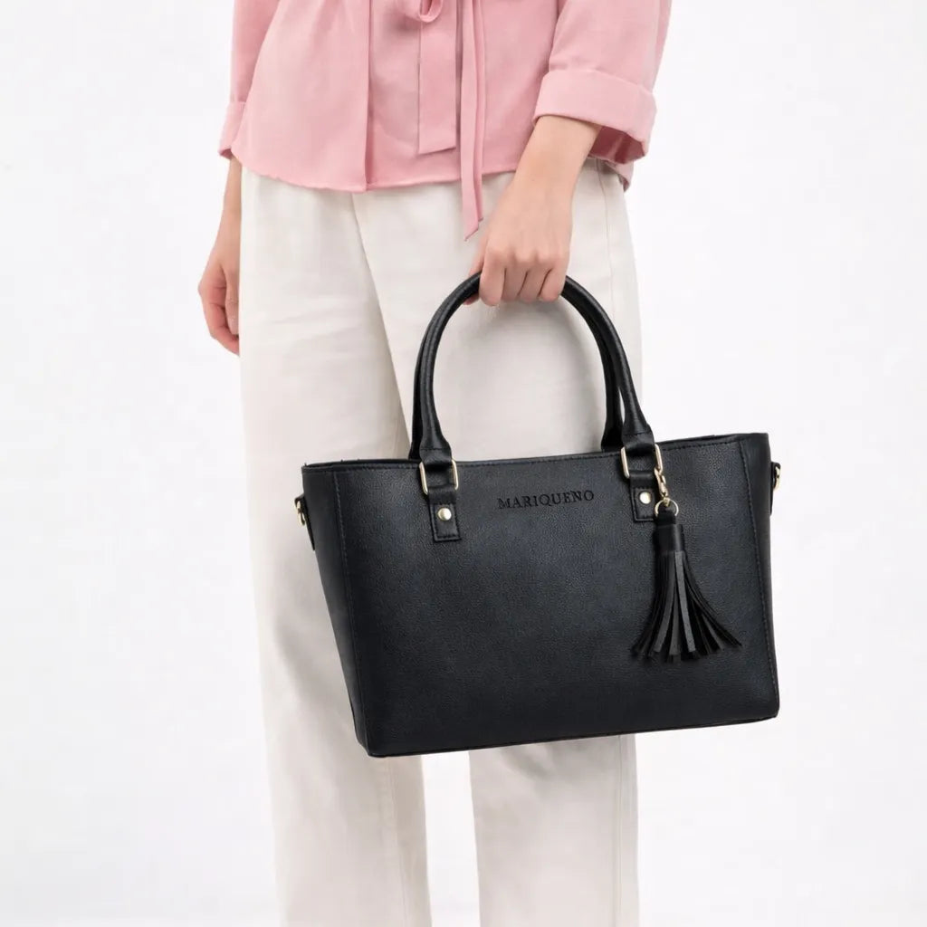 Black handbag with a brand logo held by a person wearing a pink jacket and white pants on a white background
#color_black