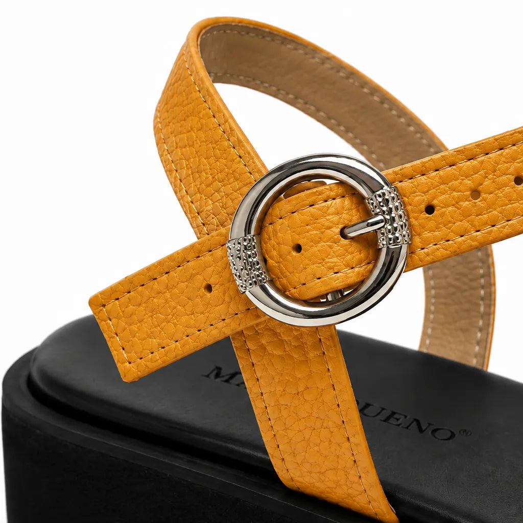 Close-up of a tan pebbled leather sandal strap with a silver-tone metal O-ring buckle, shown on a black platform heel against a white background.
#color_tan