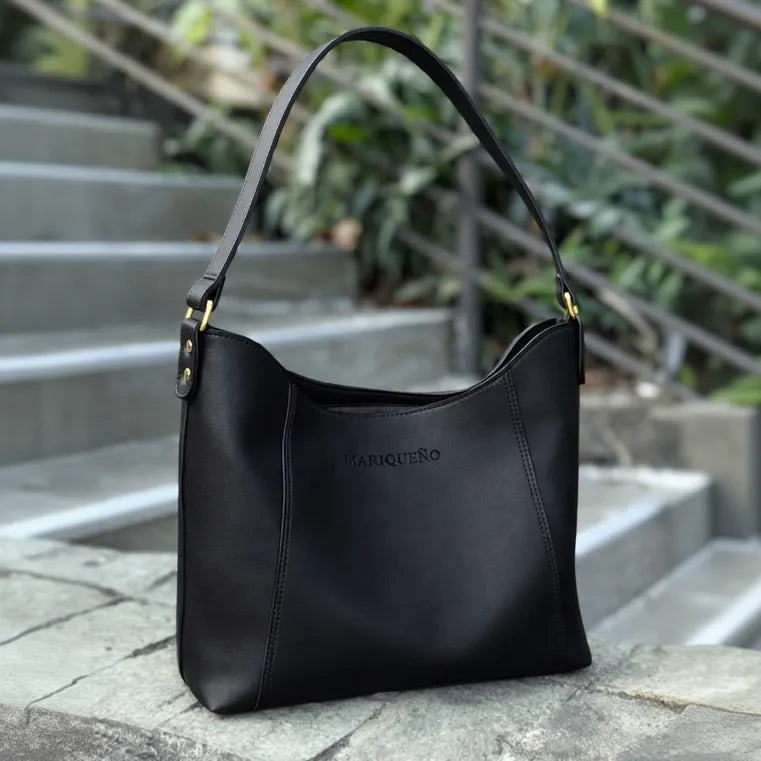 Black leather handbag with 'MARIQUENO' branding on a stone surface with steps and plants in the background.
#color_black