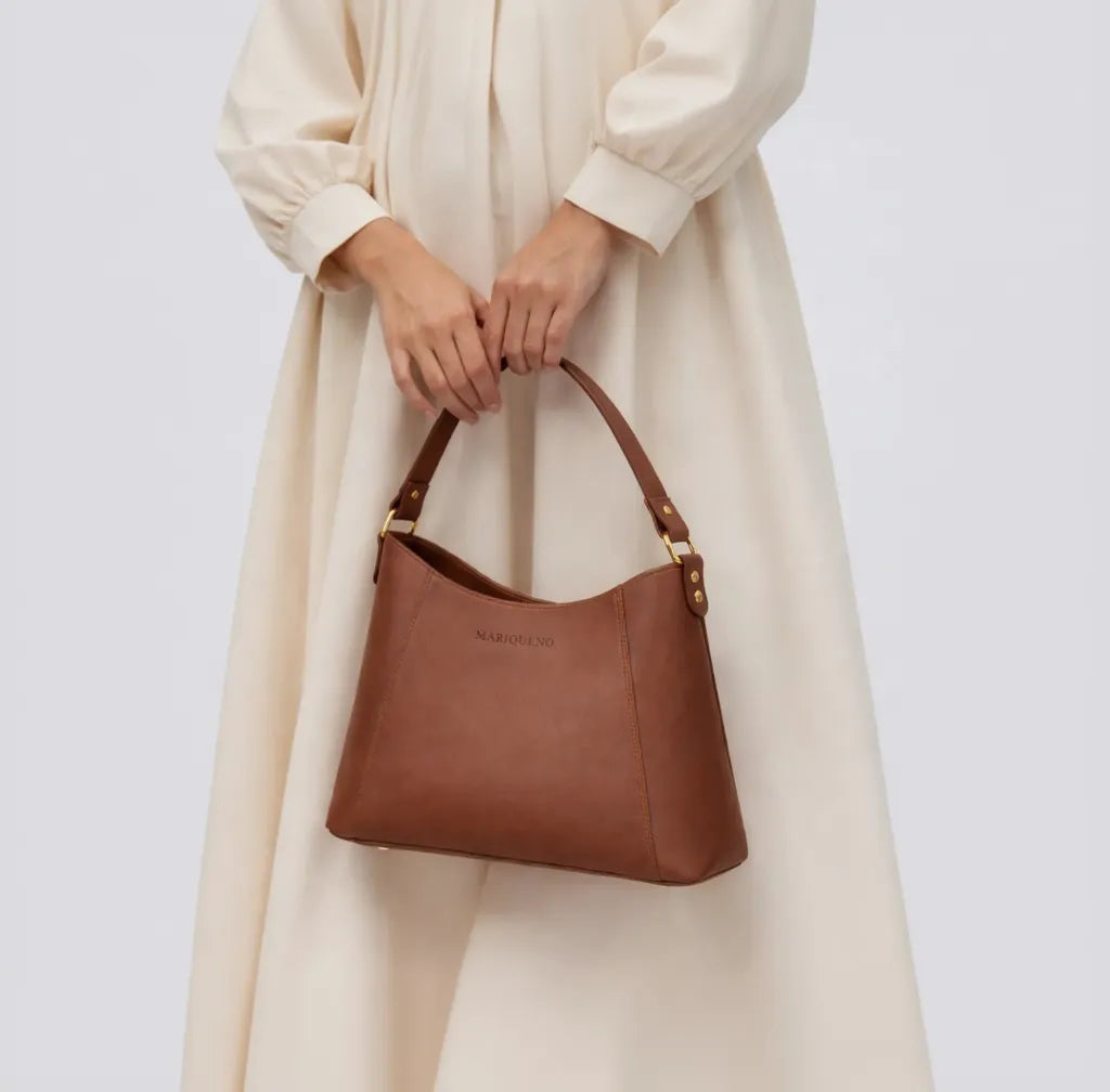 Brown leather handbag held by a person wearing a beige coat on a white background
#color_choco brown