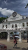 A person carrying a white umbrella walks in front of the large white Markina City gate under a cloudy blue sky. Large overlaid text reads 'CERTIFIED Marikina Made'.
